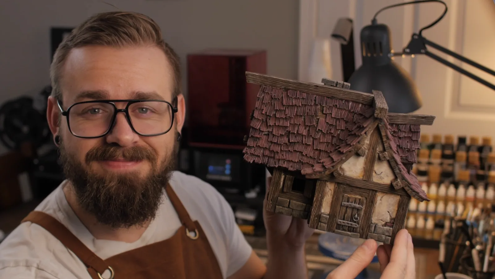 Nicholas holding up a finished miniature cottage with a shingled roof.